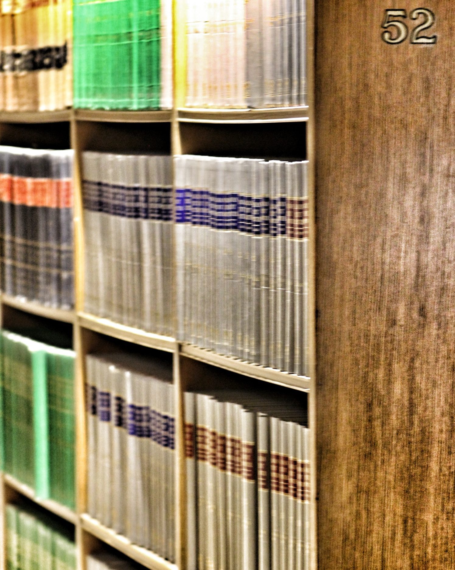 Rzędy oprawnych tomów z przepisami i komentarzami na półkach biblioteki prawniczej.